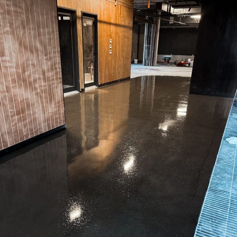 A hallway with polished concrete floors, wooden wall paneling on the left, and several utility items in the background.