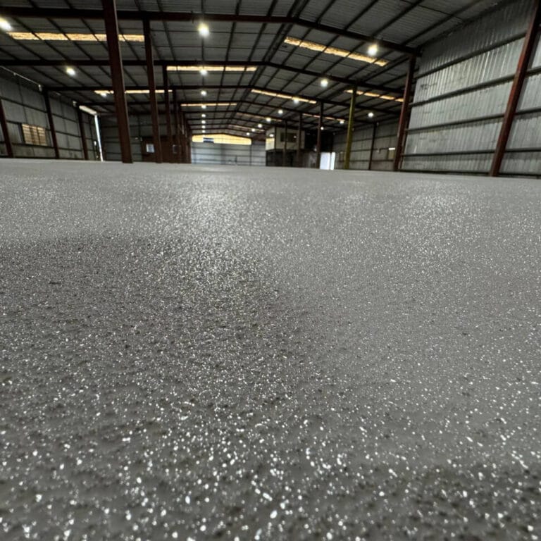 Close-up view of a concrete floor with a shiny, textured surface inside a large, empty warehouse.