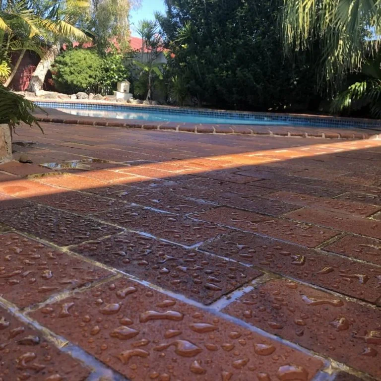 A waterproofed brick patio with water droplets on it next to a swimming pool.