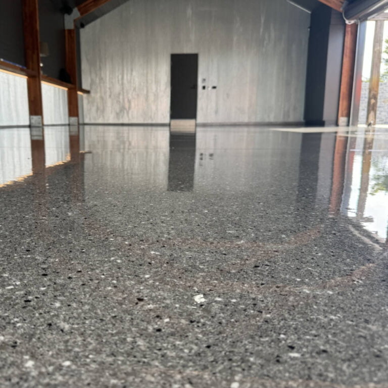 A close-up view of a polished concrete floor in an empty room with a textured gray wall and a door in the background.