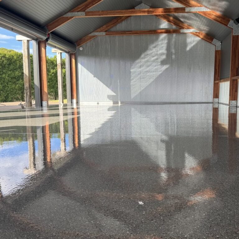 A newly constructed building with an empty interior; a glossy black floor reflecting sunlight through the open walls and roof structure.