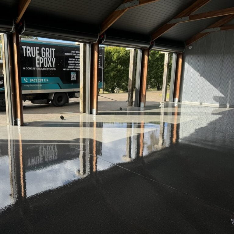 A polished concrete garage floor reflects light, with a truck featuring "True Grit Epoxy" parked outside under an open garage door.