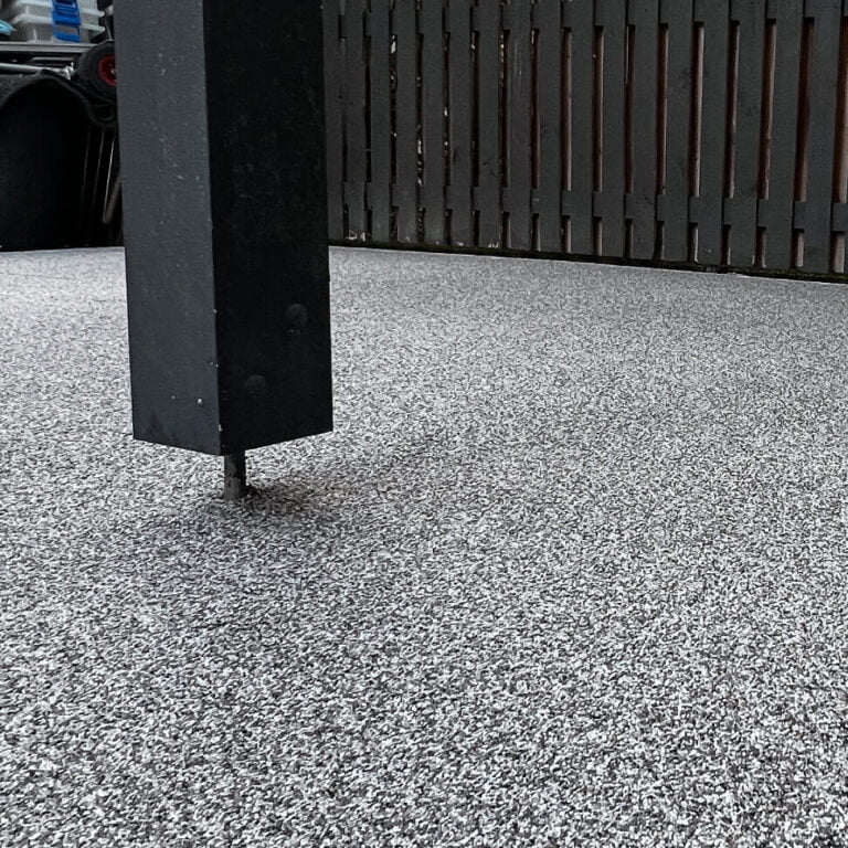 Close-up of a black metal post on a speckled gray surface, with a dark wooden fence in the background.