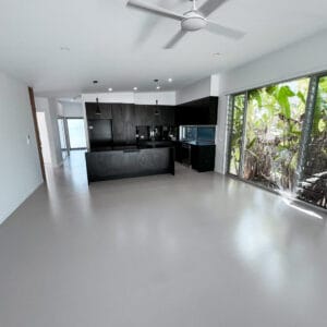 Modern open-plan kitchen and living area with dark cabinets, large windows, overhead fans, and polished light flooring.