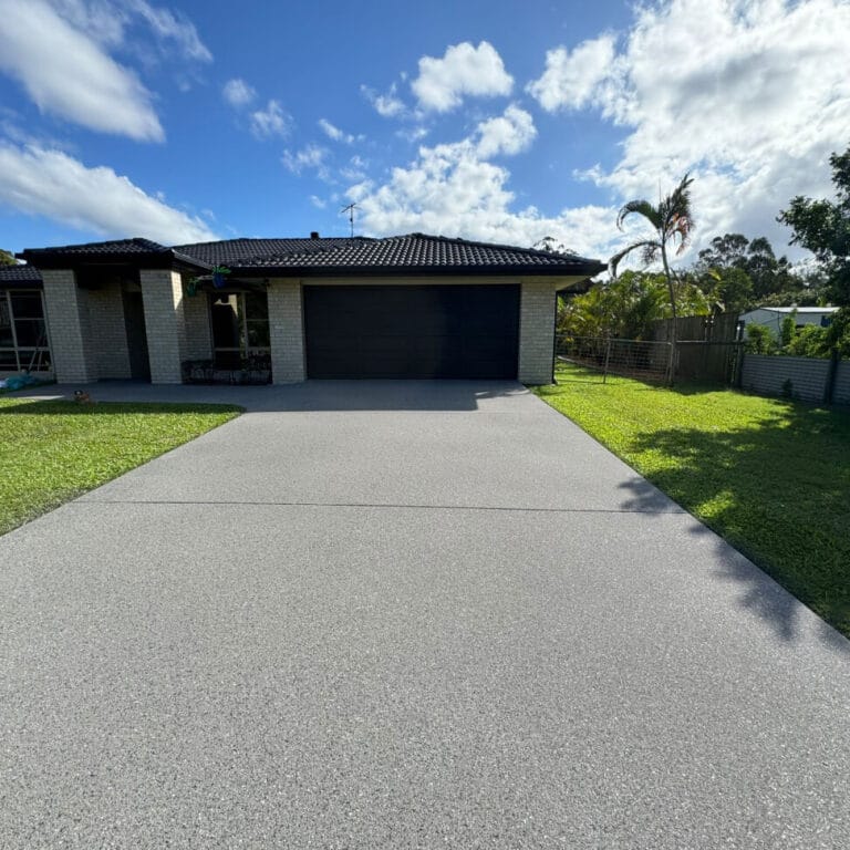 A modern single-story house with a dark roof and garage, surrounded by a green lawn and a clear sky with scattered clouds.