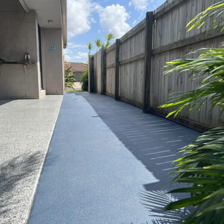 A backyard with a blue concrete walkway.