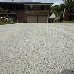 Low-angle view of a two-story wooden house with a wide driveway leading to closed double garage doors.