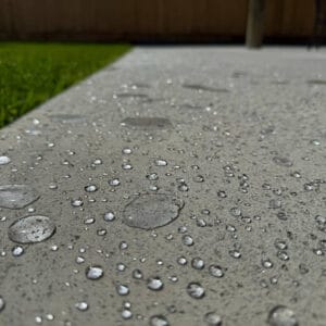 Water droplets scattered on a concrete surface with grass visible in the background.