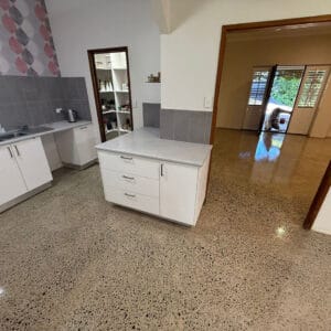 A kitchen with white cabinets and drawers, grey tile backsplash, polished stone floor, an open pantry, and a view into an adjoining room with open doors to the outside.