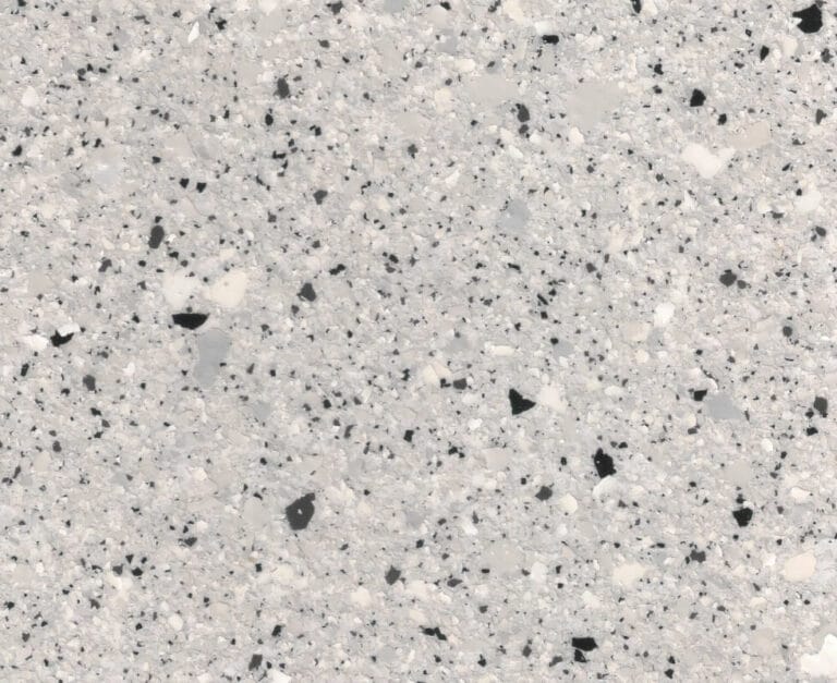 Close-up of a speckled gray surface with black, white, and light gray spots. The texture resembles terrazzo flooring.